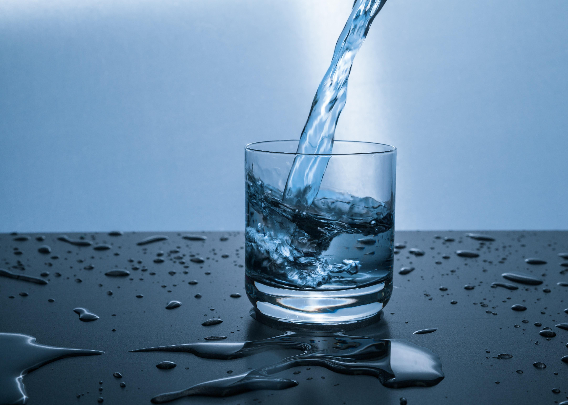 Acqua pura versata in un bicchiere di vetro su superficie scura con riflessi e gocce